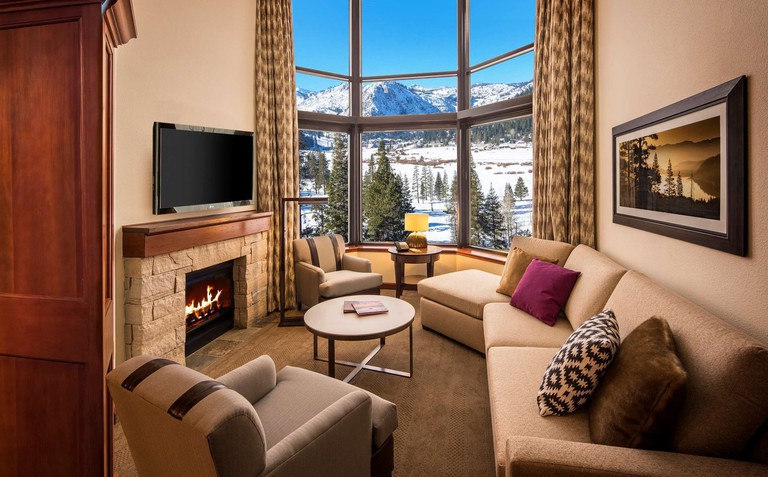 A cosy living area at Resort at Squaw Creek, with sofas, armchairs, a small table, a TV, fire place and windows with snowy views