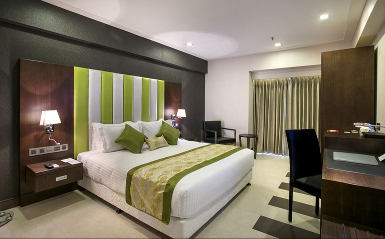 A comfortable with room with one bed, a striped bedhead and a desk with a chair at the Platinum Grand