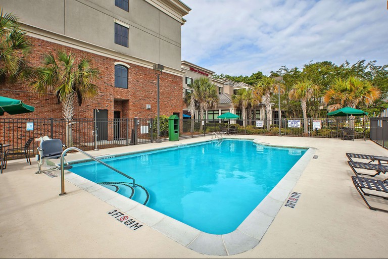 Rectangular concrete pool area at the Hilton Garden Inn in Beaufort, with small palm trees around the edge, and a scattering of black sun loungers.