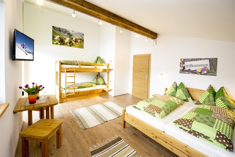 A light-filled bedroom with cheerful green-and-brown bedding on the large bed and a set of bunk beds in an apartment at the Alpenhof Grafleiten