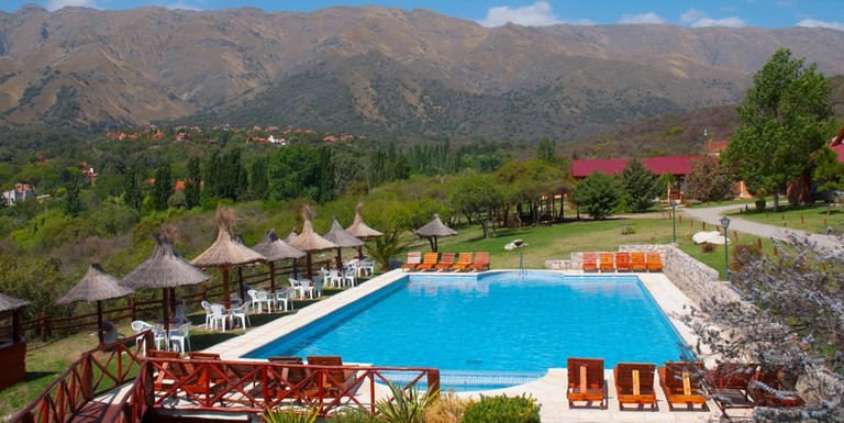 The outdoor pool with lounge chairs and palapas at Altos del Sol Spa and Resort, surrounded by woodlands and mountains behind