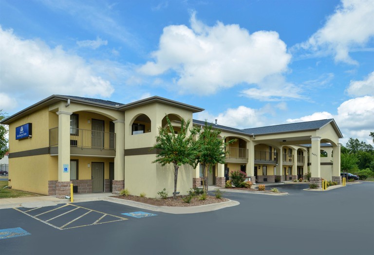 The sand-colored exterior of Americas Best Value Inn and Suites University Ave, with trees, plants and parking