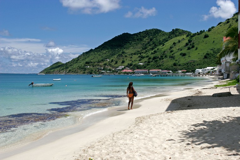 Woman in orange bikini with bag strolls at water edge Grand Case beach St Martin