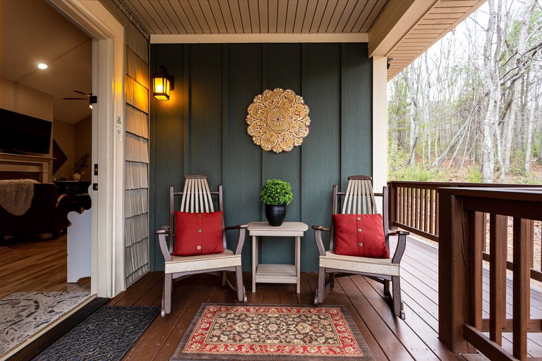 Two wooden chairs on the wooden porch of Asheville Cottages, North Carolina; a large, wall-mounted TV can be seen inside through the doorway