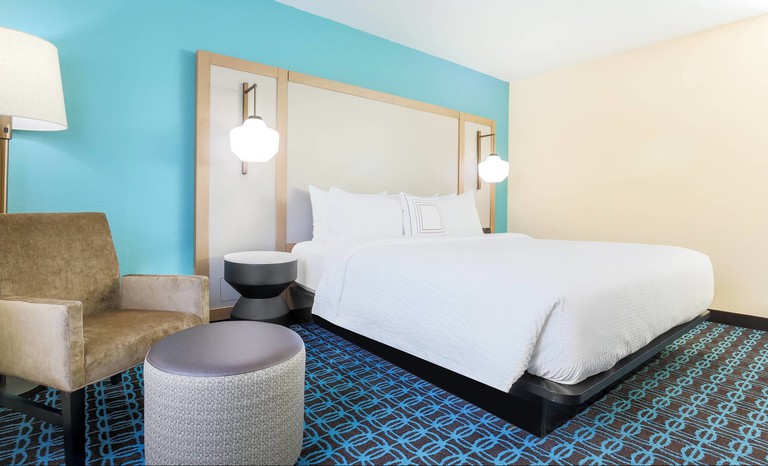 A guest room with one king-size bed with an oversized headboard, a chair, a footstool and side tables at the Fairfield Inn and Suites Houston Humble
