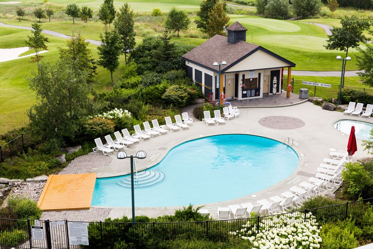 Overhead view of Brookstreet Hotel's outdoor pool and jacuzzi area with white lounge chairs and golf course in the background