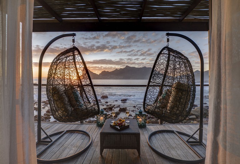 A pair of egg chairs on a wooden balcony overlooking the ocean in Cape Town