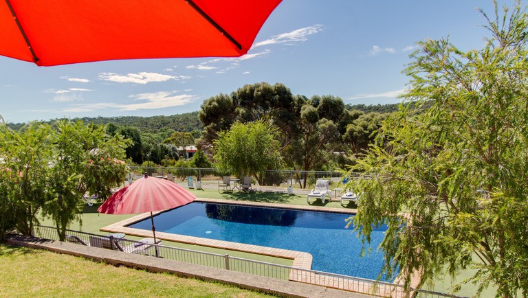 Loungers and chairs by an outdoor pool with forest views at Clare Valley Motel