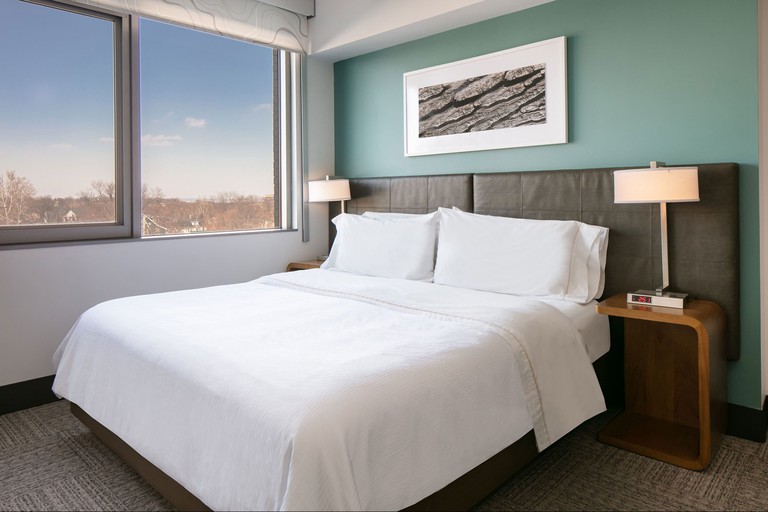 Double bed with white bed linen in front of a green wall at Element Omaha Midtown Crossing