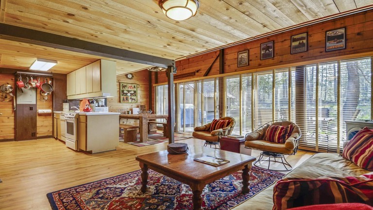 Bright, woodsy open-plan living-dining space with windows out to woods of Cluster Cabin 26