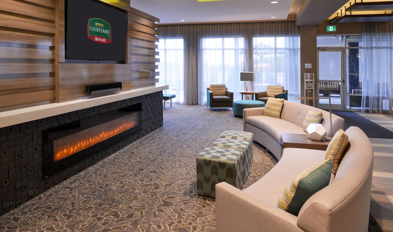 A communal lounge with a curved couch, TV and fireplace at Courtyard by Marriott Saskatoon Airport