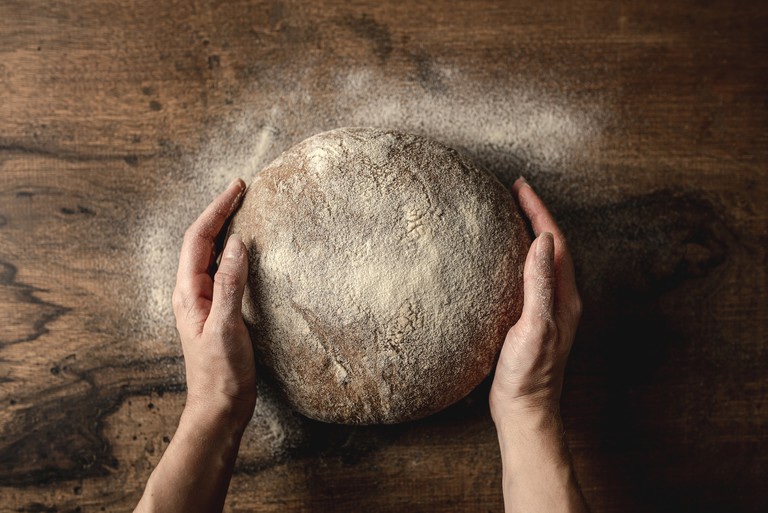 Bakers hands cup a round, floury loaf of heritage grain bread.