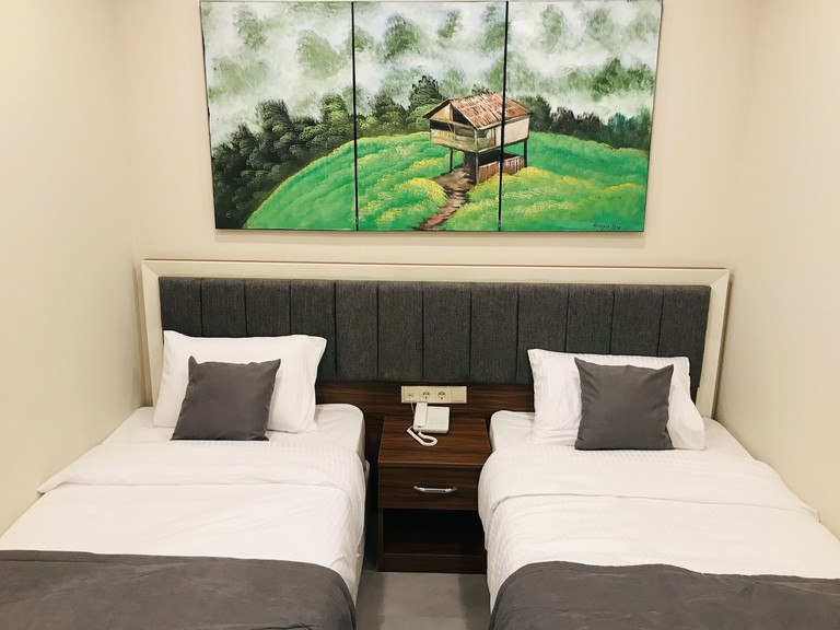 Two adjacent single beds in white-painted room with pastoral canvas artwork on wall at Deryaman Hotel Trabzon