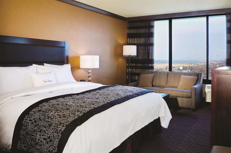 A large bed in a room at DoubleTree by Hilton Cleveland Downtown, with a couch by tall windows looking towards open water