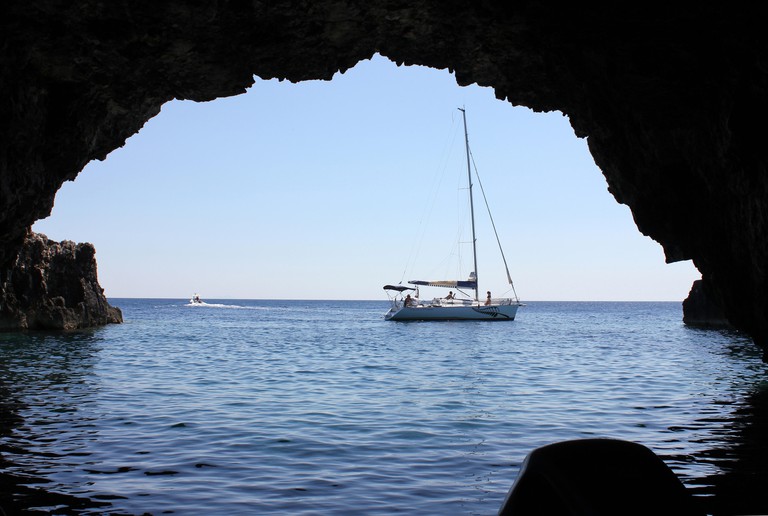 A view looking out of the dark mouth of the Green Cave, with a small sailing boat floating just outside.