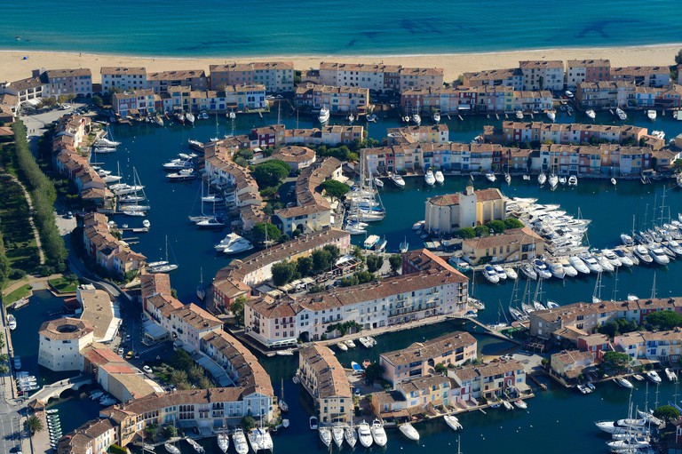 An aerial view of Port Grimaud showing its network of canals, which are flanked by traditional buildings and white motorboats.