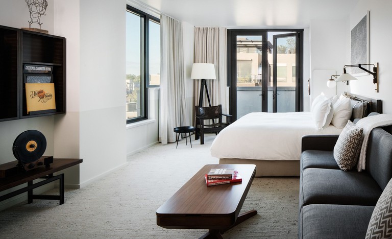Modern room with a double bed, dark grey couch, wooden coffee table, beige carpeted-floors and a private balcony at Halcyon Hotel Cherry Creek