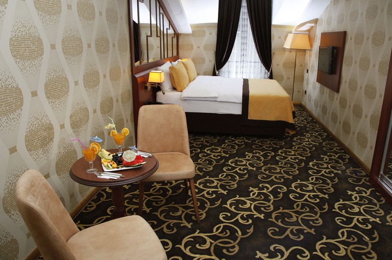 Double bed facing wall-mounted TV in carpeted room with two upholstered chairs by a small table at Grand Vuslat Hotel