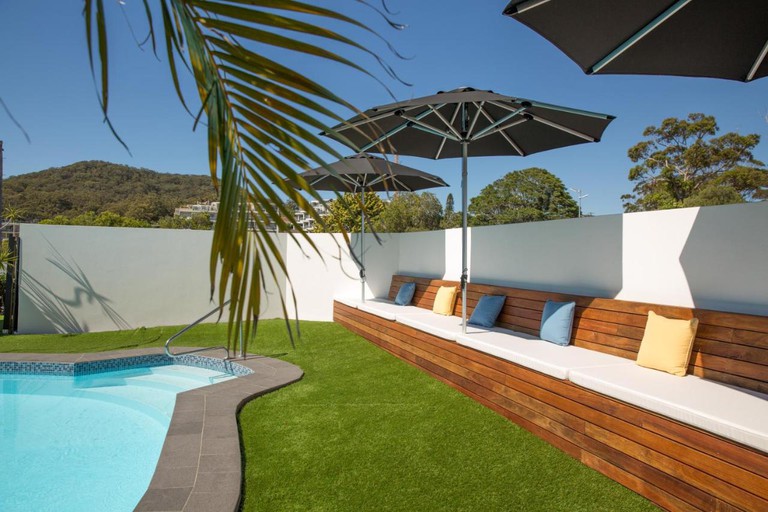 Shaded, cushioned bench seating next to artificial grass and an outdoor pool with steps and handrail at Hotel Nelson