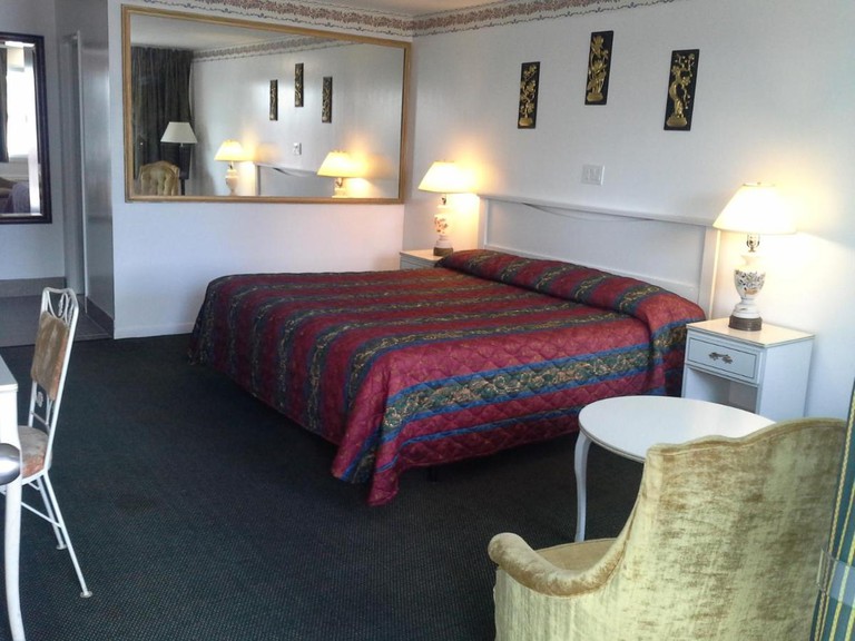 A large bed in an Inn Towne Motel room, next to a wall with a large mirror