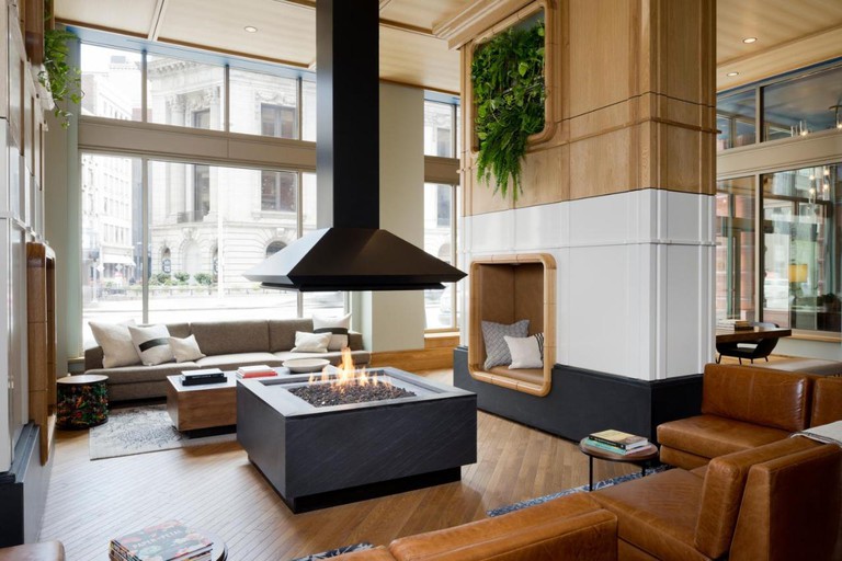 The stylish Living Room at the Kimpton Schofield Hotel with an open firepit in the center, sofas and seating in nooks
