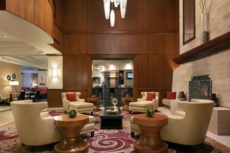 Lobby at Marriott Denver Airport at Gateway Park, with cream armchairs, tall wooden coffee tables and a swirly red rug.