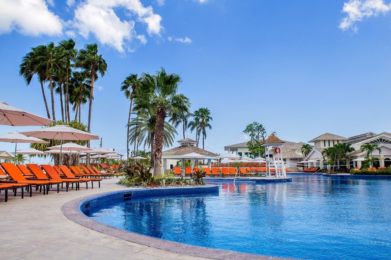 An outdoor pool at Moon Palace Jamaica with palm trees, parasols and orange sun loungers