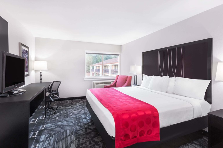 A king business suite dressed mostly in black and white, with a pop of red on the bed and red armchair, at the Ramada by Wyndham Tuscaloosa