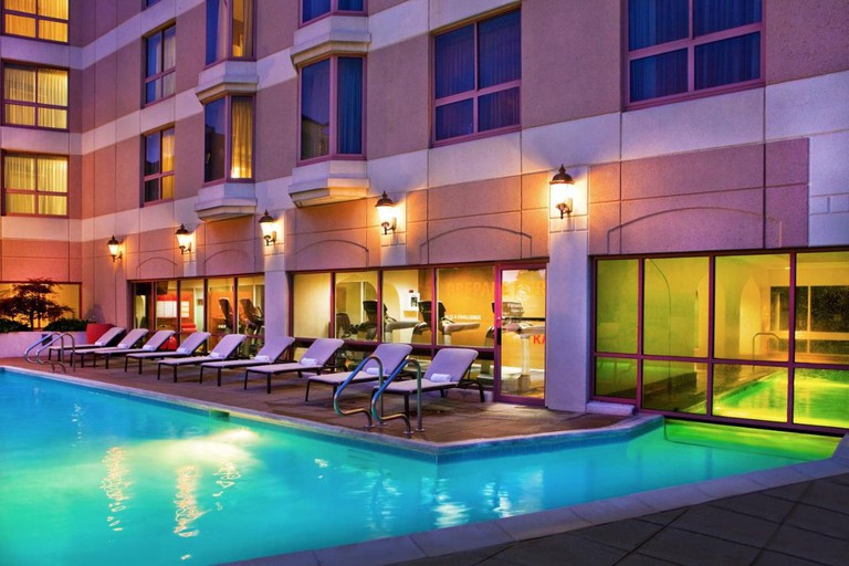 Outdoor swimming pool surrounded by sunbeds and overlooked by an indoor gym at Sheraton Suites Country Club Plaza