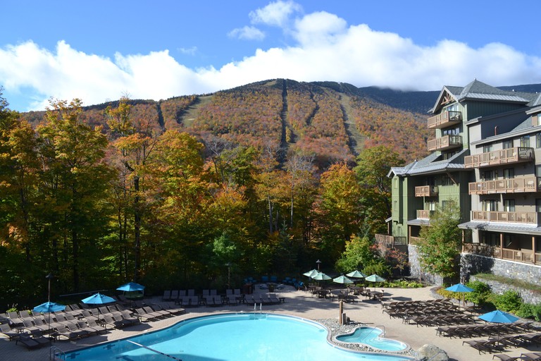 The large pool surrounded by loungers, umbrellas and towering trees at the Lodge at Spruce Peak