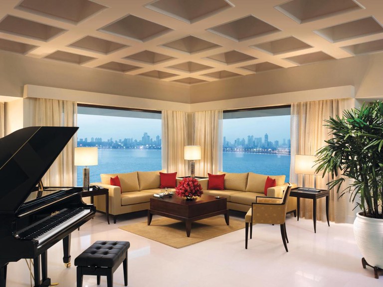 Lounge area with a corner sofa and a piano overlooking the water at The Oberoi Mumbai