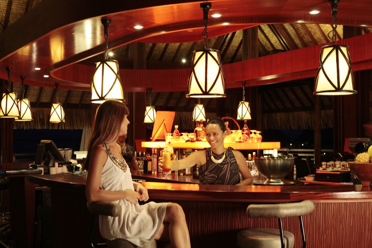 A woman serves another woman a cocktail at the lamp-lit Vue Bar at the Sofitel Kia Ora Moorea Beach Resort