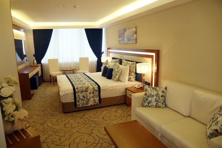 Double bed, sofa, two chairs and a wall-mounted TV in cream room at Yol Is Holiday Hotel Trabzon