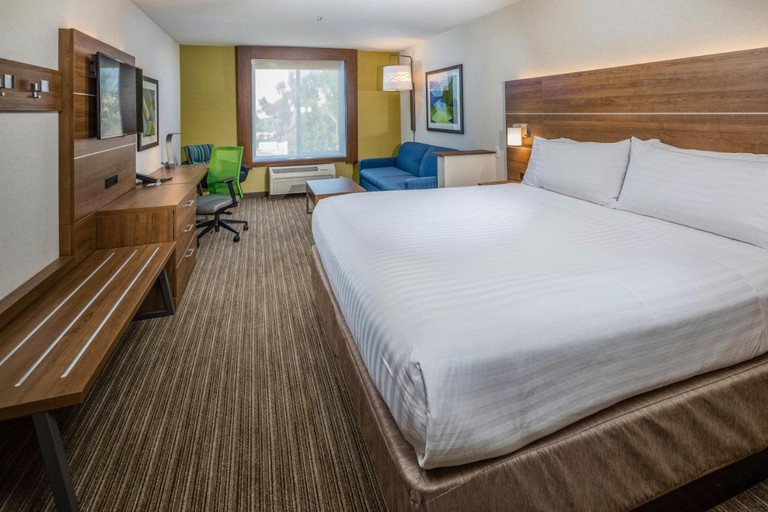 A large bed with white linen and a wooden headboard in a room with a separate seating area at Holiday Inn Express Hotel & Suites Modesto-Salida, an IHG Hotel