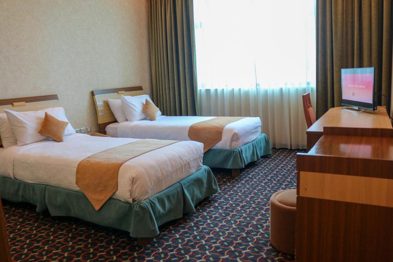 Two single beds, and a TV on a wooden desk in an Elite Grande Hotel room