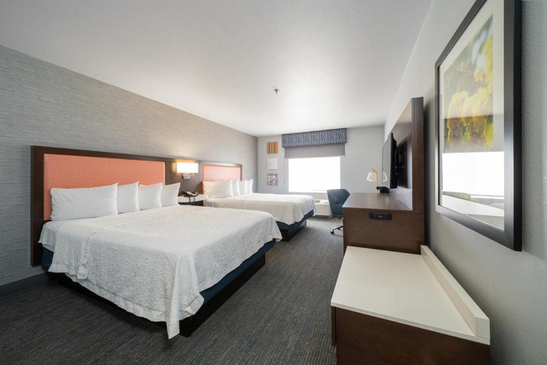 A room with two beds, with pink headboards, and dark-wood furniture at Hampton Inn & Suites Modesto