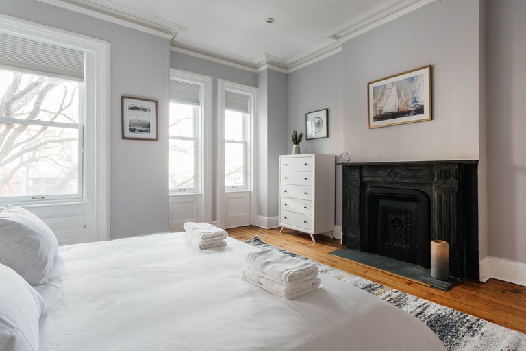 A bedroom at City's Escape with a double bed with white linen, wooden floors, white furniture and a black fireplace