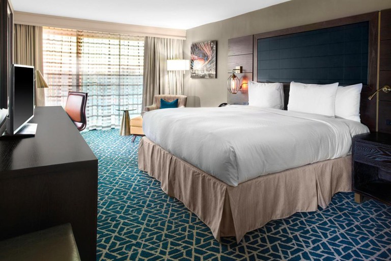 A hotel room at DoubleTree by Hilton Hotel Arlington DFW South with a double bed, blue patterned carpet, brown desk with TV and cream chair