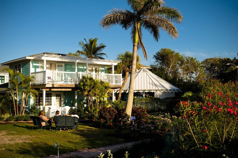People sit on chairs in the garden outside Tropic Isle at Anna Maria Island Inn, with tall palm trees and other flora