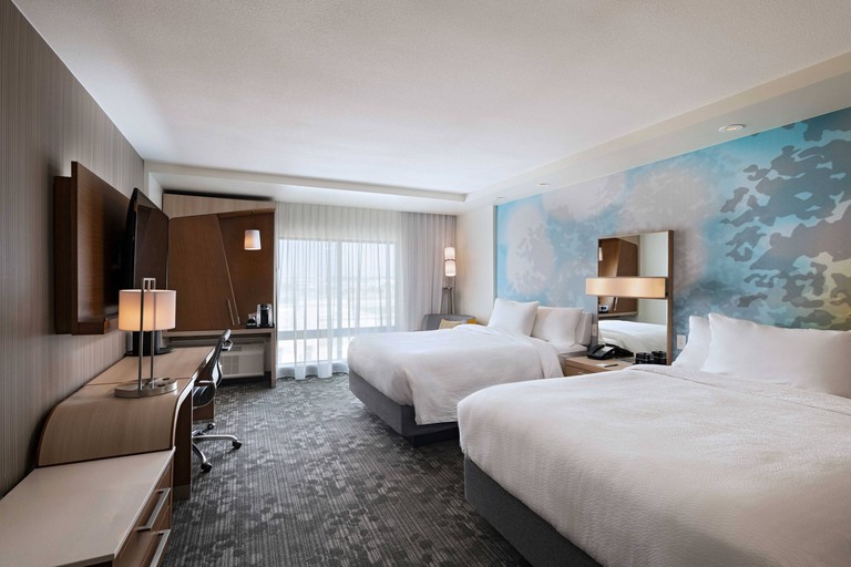 Two double beds against a blue-patterned accent wall in a room with a grey carpet, desk and flat-screen TV at Courtyard by Marriott Dallas Grand Prairie