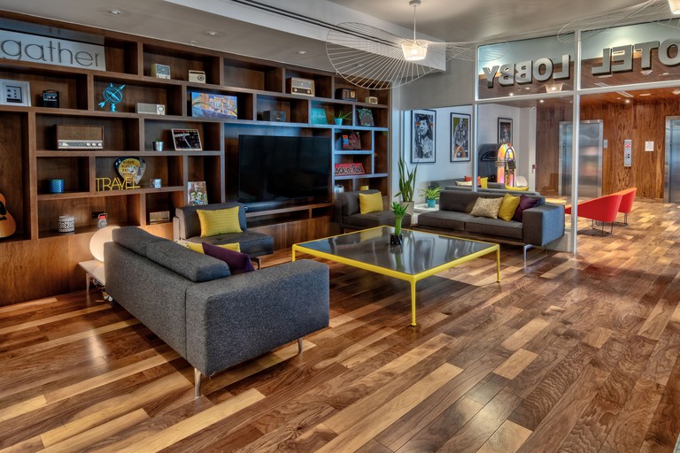 Modern lobby of Hotel Indigo Memphis Downtown featuring a wooden bookcase, a flat screen TV, grey couches, a large coffee table and a jukebox by the elevator