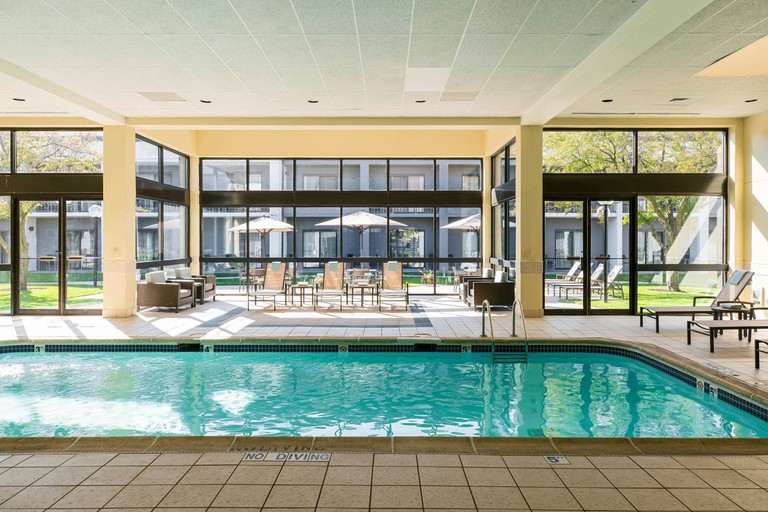 Indoor pool with steps and handrail at Courtyard Chicago Naperville; several loungers and sofas on the tiled area around it