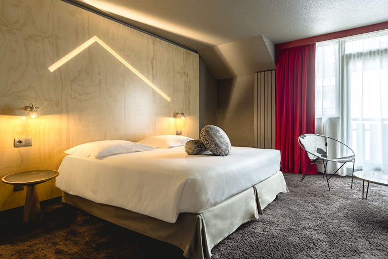 A modern bedroom in Hôtel Le Refuge Des Aiglons, with a fluffy carpet, light-wood wall and cow-print seating