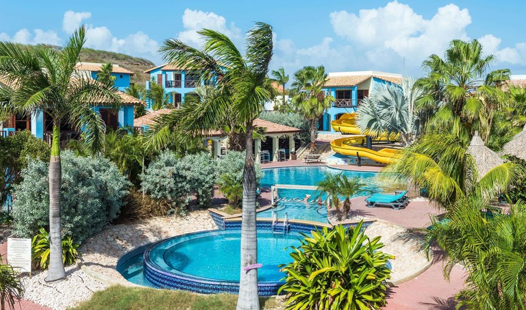 Lush pool area with water slide at Kunuku Aqua Resort surrounded by Caribbean blue buildings
