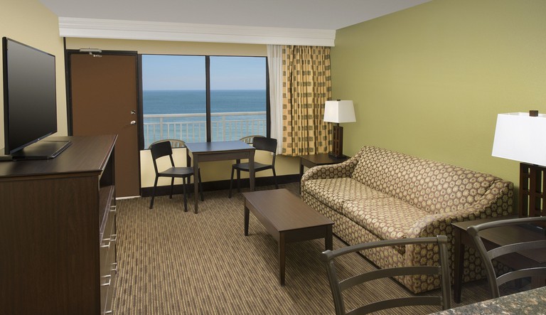Brown patterned couch in a room with green walls, brown carpet, ocean views and a flat-screen TV at Four Points by Sheraton Virginia Beach Oceanfront