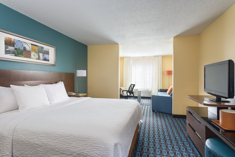 Double bed facing TV in suite with sofas, desk, desk chair and radiator at Fairfield Inn and Suites Chicago Naperville/Aurora