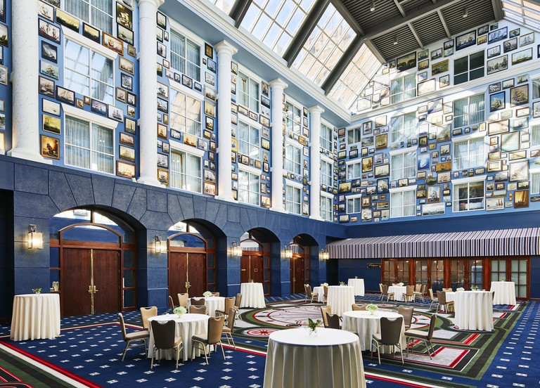 Unusual atrium dining area at Graduate Annapolis, decorated in red, white and blue, and overlooked by four tall walls dense with windows and seafaring paintings.