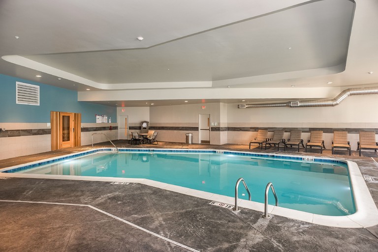 An indoor swimming pool at Holiday Inn & Suites - Joliet Southwest surrounded by gray-tiled floors and sunbeds
