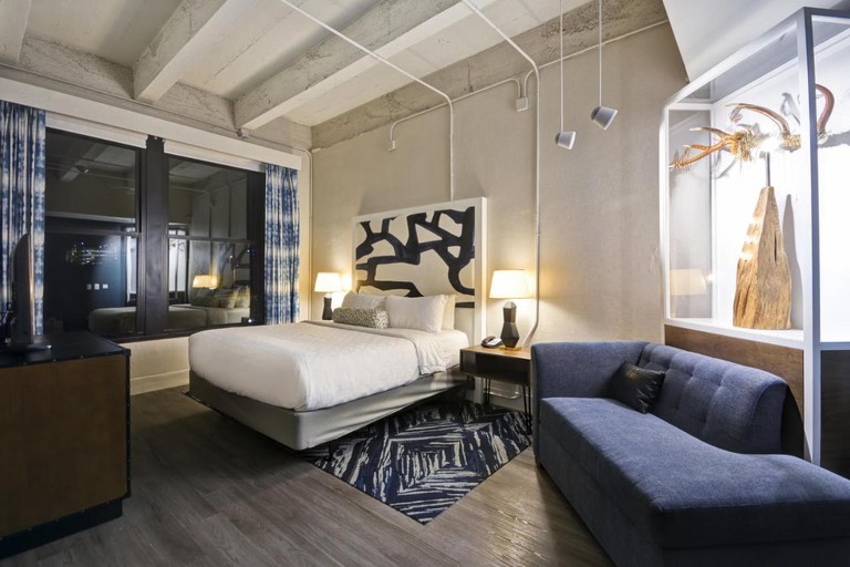 Industrial-style room at Hotel Indigo Kansas City with double bed, patterned headboard, blue chaise longue and artwork display