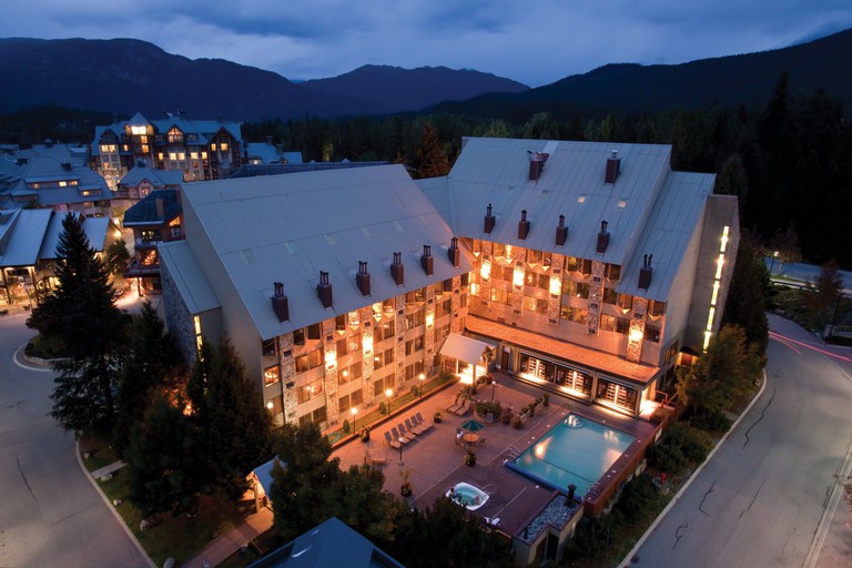 Mountainside Lodge as seen from above in the evening, with an outdoor pool out front and mountains behind
